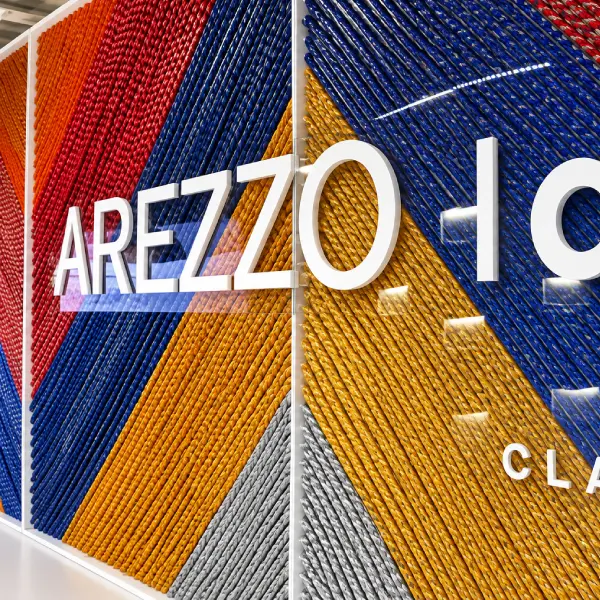 Painel em acrílico com letras "Arezzo lab" sobre fundo de fios coloridos
